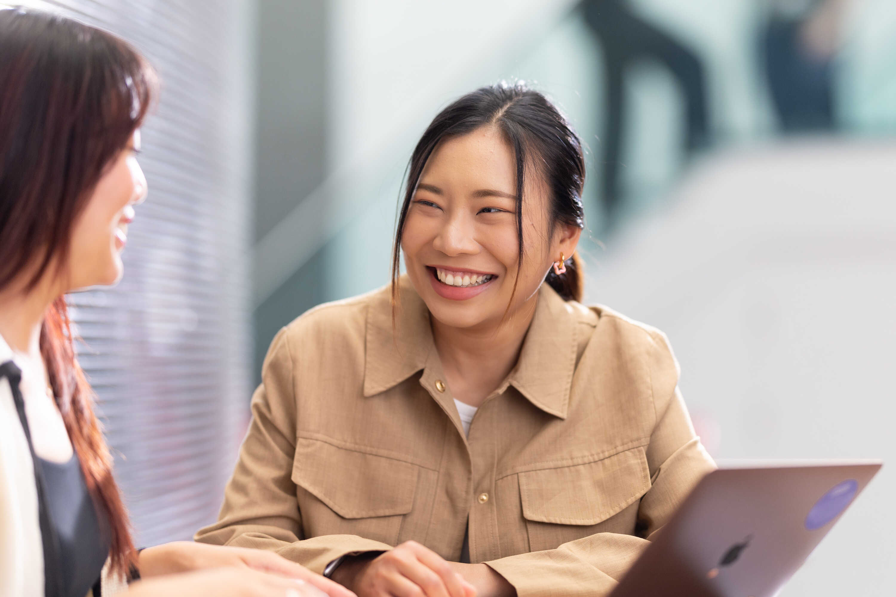 Smiling student with laptop sat outside, looking at another student