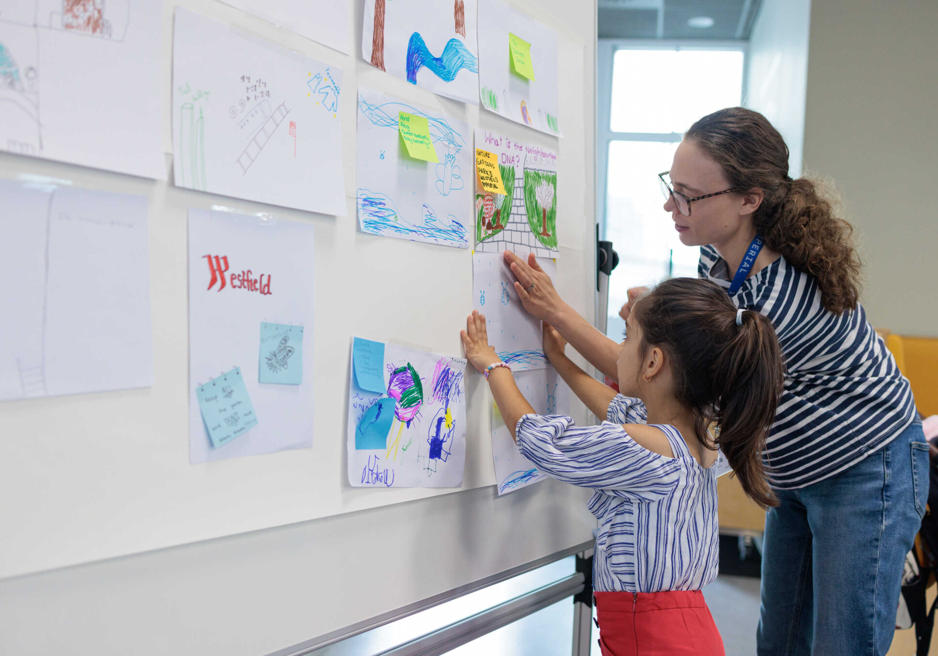 A woman and a child pin drawings up on a whiteboard together